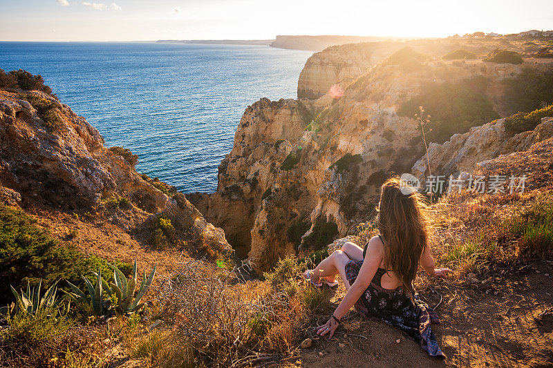 在葡萄牙阿尔加维的Ponta da Piedade悬崖边看日落的女人